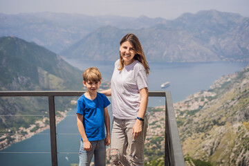 Fototapeta na wymiar Mother and son travellers enjoys the view of Kotor. Montenegro. Bay of Kotor, Gulf of Kotor, Boka Kotorska and walled old city. Travel to Montenegro concept. Fortifications of Kotor is on UNESCO World