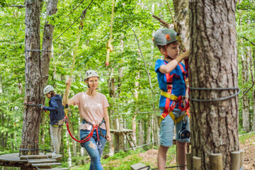 Naklejka na ściany i meble Mother and son climbing in extreme road trolley zipline in forest on carabiner safety link on tree to tree top rope adventure park. Family weekend children kids activities concept Portrait of a