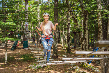Naklejka na ściany i meble Happy women girl female gliding climbing in extreme road trolley zipline in forest on carabiner safety link on tree to tree top rope adventure park. Family weekend children kids activities concept