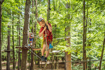 Naklejka na ściany i meble Happy child in a helmet, healthy teenager school boy enjoying activity in a climbing adventure park on a summer day Portrait of a disgruntled girl sitting at a cafe table