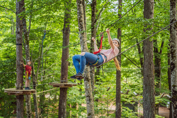 Naklejka na ściany i meble Mother and son climbing in extreme road trolley zipline in forest on carabiner safety link on tree to tree top rope adventure park. Family weekend children kids activities concept Portrait of a