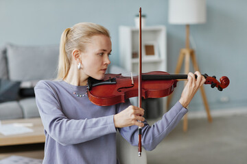 Side view portrait of elegant blonde woman playing violin at home or in music studio
