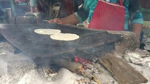 Poor woman cooking tortillas on a metal griddle in her humble home in Managua, Nicaragua