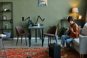 Wide angle shot of young man playing electric guitar in home music studio, copy space