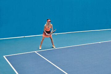 Horizontal extreme long shot of young professional tennis player standing on court holding racket getting ready to strike ball