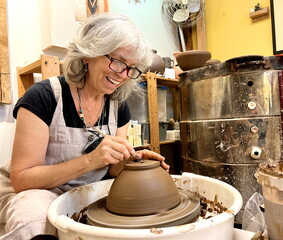 Beautiful adult explored her woman sculpts a vase from clay She wears black-framed glasses and gray hair black T-shirt and a gray apron Pottery is a favorite pastime and relaxation Pleasure and joy
