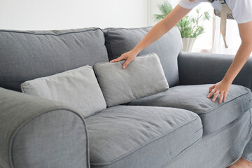 Woman cleaning and arranging sofa cushions at home.