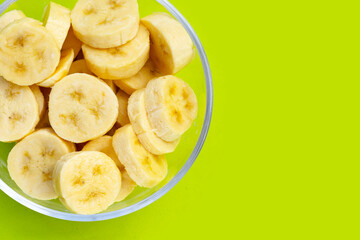 Banana slices in glass bowl on green background
