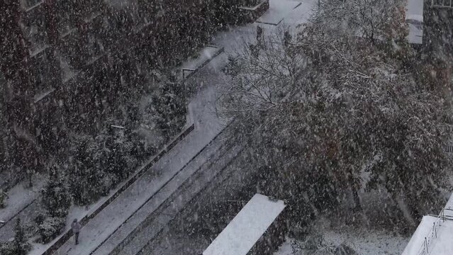 Aerial view of empty road, pedestrians, trees and buildings covered in snow during winter season and first snowfall in the city. Slow motion Video footage