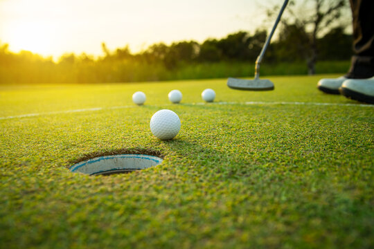 golfer training putting a golf ball into a last hole on the green, golf course on summer sunset evening time with copy space