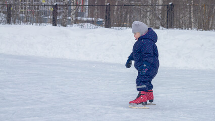 Fototapeta na wymiar Baby girl skating in winter on an outdoor ice rink on ice