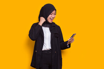 happy young asian beautiful muslim woman using mobile phone isolated on yellow background
