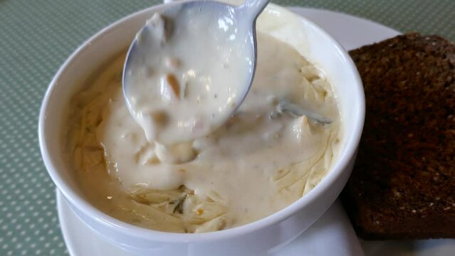 Delicious creamy seafood chowder bowl with spoon stirring and slice of brown bread on the side