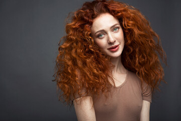 Portrait of a curly-haired red-haired woman on a dark gray background. The woman looks directly into the camera. With a space to copy. High quality photo
