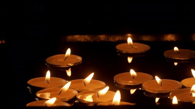 Close-up of illuminated candles floating in water. Burning decorative lights in artificial pond. Beautiful lit flames in dark room.