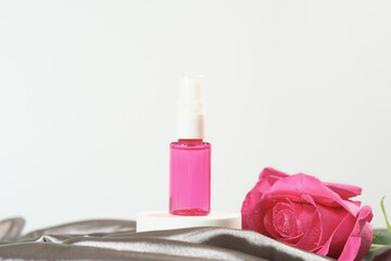 textile freshener in a plastic sprayer on white pedestal next to rose flower and silk satin sheet....