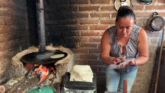 Mujer mexicana torteando maza de ma&iacute;z en un metate y una estufa de le&ntilde;a para hacer tortillas