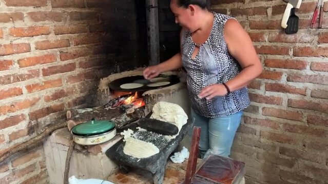 Mujer mexicana torteando maza de ma&iacute;z en un metate y una estufa de le&ntilde;a para hacer tortillas