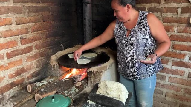 Mujer mexicana torteando maza de ma&iacute;z en un metate y una estufa de le&ntilde;a para hacer tortillas