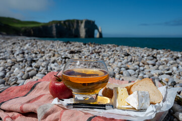 Lunch on pebbles beach of Etretat, french cheese camembert and apple cider drink with chalk cliffs and Atlantic ocean on background, Normandy, France