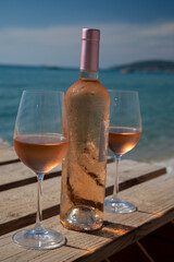 Glasses and bottle of cold rose wine from Provence served outdoor on wooden yacht pier with view on blue water and white sandy beach Plage de Pampelonne near Saint-Tropez, France