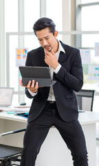 Millennial Asian professional successful bearded male businessman in formal suit sit on table browsing surfing internet via tablet computer in company office meeting room while colleagues discussing