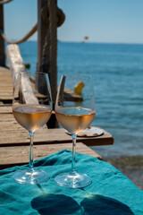 Glasses of cold rose wine from Provence served outdoor on wooden yacht pier with view on blue water and white sandy beach Plage de Pampelonne near Saint-Tropez, France