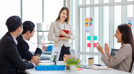 Millennial Asian professional successful young cheerful female  businesswoman speaker lecturer in formal suit standing smiling pointing graph chart information document on glass board in meeting room