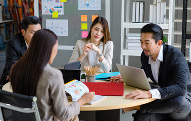 Millennial Asian professional successful male businessmen and female businesswomen colleagues in formal suit sitting discussing brainstorming together on round table in company office meeting room