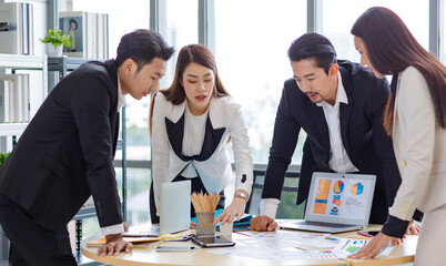 Millennial Asian professional successful male businessmen and female businesswomen colleagues in formal suit standing discussing brainstorming together on round table in company office meeting room