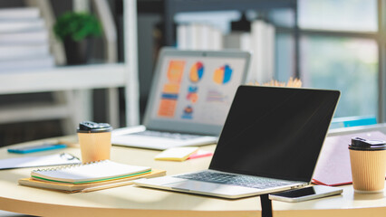 Desk full of stationary equipment, black blank screen mockup laptop notebook computer, coffee cup...