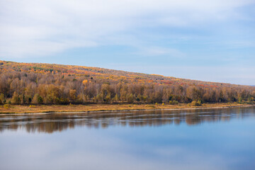 Beautiful, wide autumn river among forests and rocky shore. A calm and quiet place with autumn colors. Reflection of clouds in the water in good weather