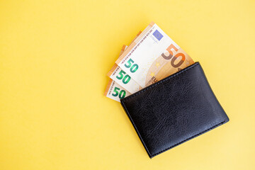Fifty euro banknotes inside a black wallet on yellow background, cash paper currency, payment, earning and savings, european currency, money and finance concept