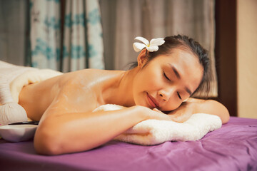 Asian woman enjoying back massage with scrub salt and cream in massage spa salon. Young girl in spa massage. Healthy treatment concept.