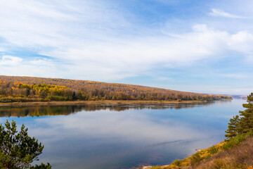 Fototapeta premium Beautiful, wide autumn river among forests and rocky shore. A calm and quiet place with autumn colors. Reflection of clouds in the water in good weather