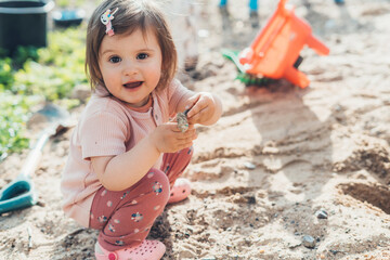 Adorable little girl on playground in sandpit discovering new things in nature. Sensory development...