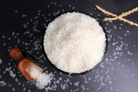 Uncooked rice with a wooden spoon. Raw surti kolam rice over black background. copy space. 