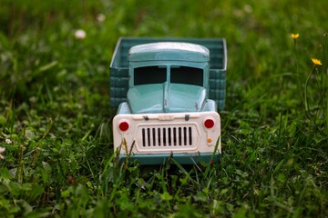 Miniature blue soviet cargo truck toy in green grass and colorful flowers of meadow