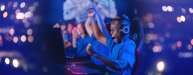 Streamer young african man rejoices in victory professional gamer playing online games computer with headphones, neon colour, soft focus - obrazy, fototapety, plakaty