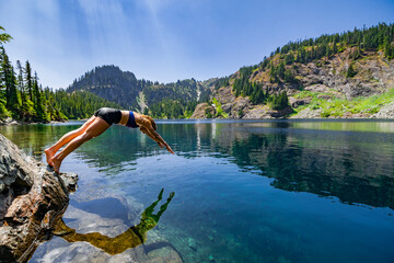 Adventurous athletic female hiker diving into an alpine lake in the Pacific Northwest.