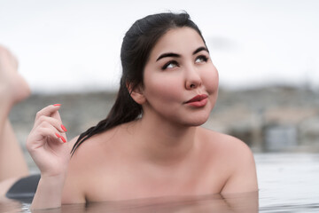 Happy plus size young woman lying down and relaxation in water of outdoors pool at spa, hot springs resorts. Feminine overweight model looking up and smiling. Healthy lifestyle, body positive concept - obrazy, fototapety, plakaty