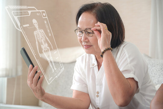 Elderly woman checking health information with hologram graphics from smartphone, close-up shot of upper half of person in living room, medical technology.