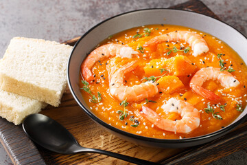 Thick autumn pumpkin soup with shrimp, sesame and thyme served with bread on a wooden tray on the table. Horizontal