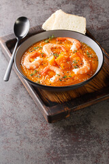 Pumpkin puree soup with shrimp, sesame and thyme served with bread on a wooden tray on the table. Vertical