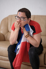Une femme blanche avec le drapeau français regardant nerveusement une compétition en se rongeant...