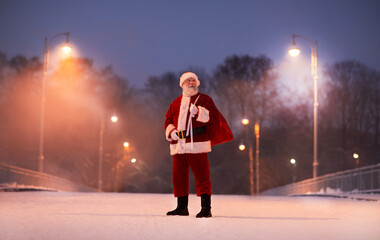 Full length portrait of traditional Santa Claus standing in city street at night on Christmas eve, copy space