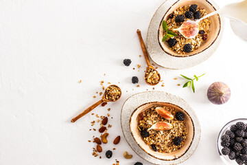top view of the white background with two modern ceramic bowls with homemade granola or muesli, with chia seeds, nuts, raisins and fruit.