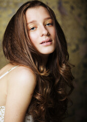 Beautiful tender young woman with long wavy hair in a white dress smiling while looking at the camera