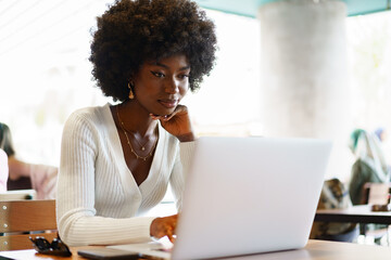 Smiling young african woman sitting with laptop in cafe