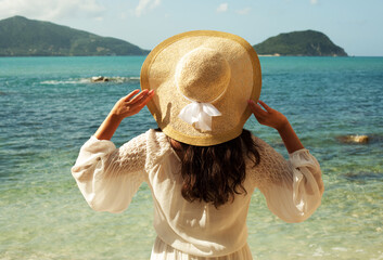 Young woman in summer white dress with straw hat looking to a sky and sea. Back view.